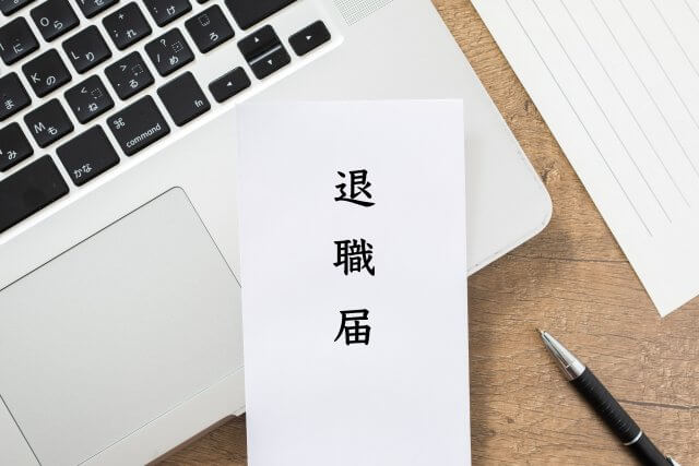 「退職届」と書かれた書類が置かれたノートパソコンとペン。退職、転職、キャリア変更、または仕事の終わりに関連するイメージ。