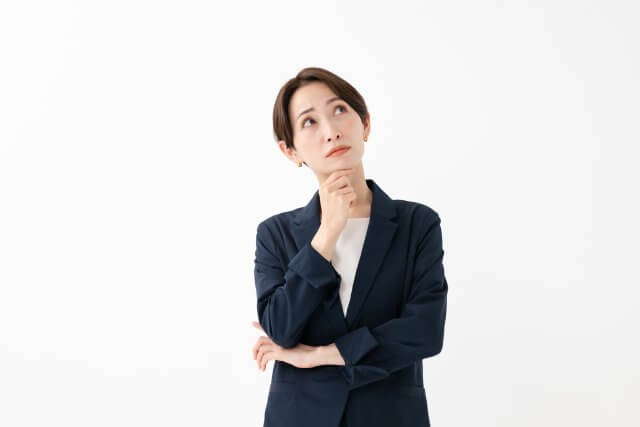 白背景の前で顎に手を当てて考え込んでいるビジネスウーマン。思考、決断、アイデア出し、または懸念を表すイメージ。